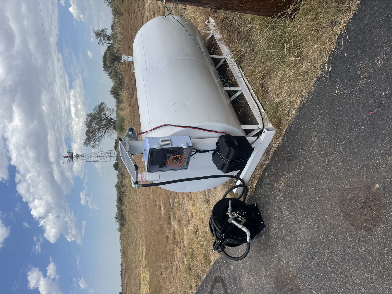 Buff Box enclosure and solar panel mounted on a horizontal 100LL tank with hose reel on the ramp